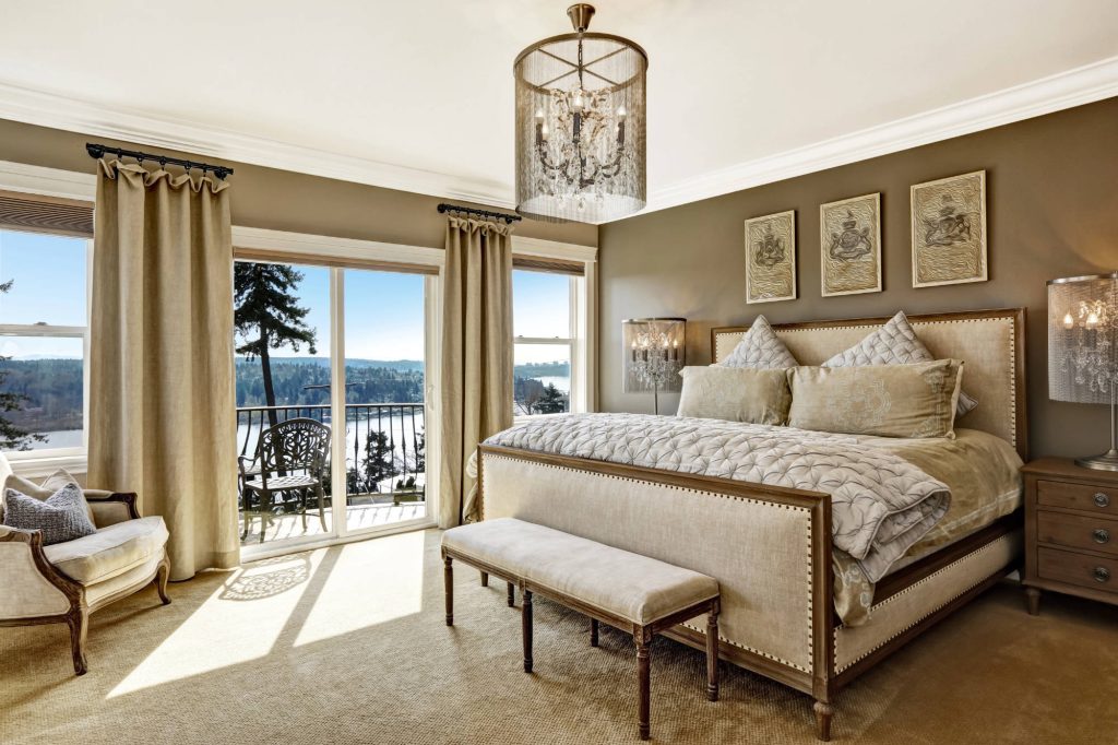 Luxury master bedroom with warm colors, large windows and elevated bed.